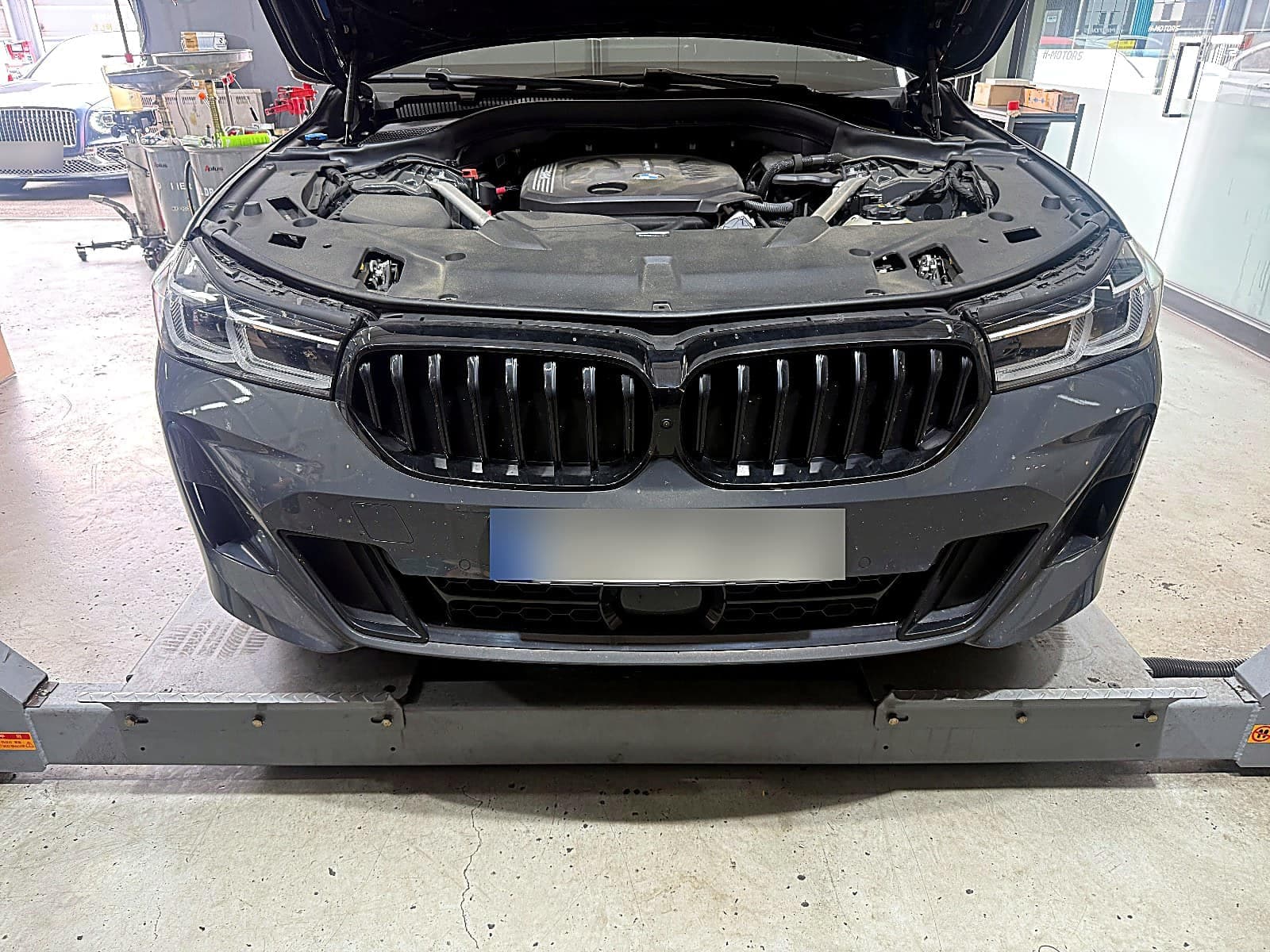 순천 H모터스 리프트에 올라간 진회색 BMW 6시리즈 GT 정면, 보닛을 연 상태